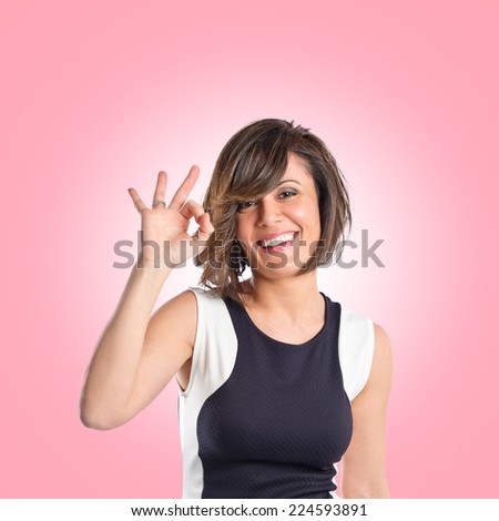 Pretty woman making Ok sign over pink background 