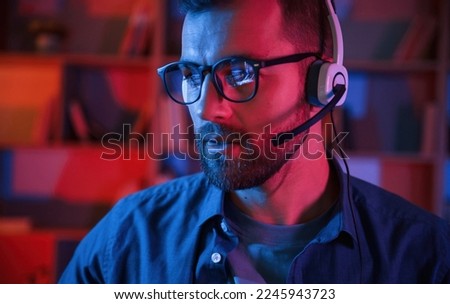 Portrait of man that is sitting by a computer indoors at home. Neon lighting.