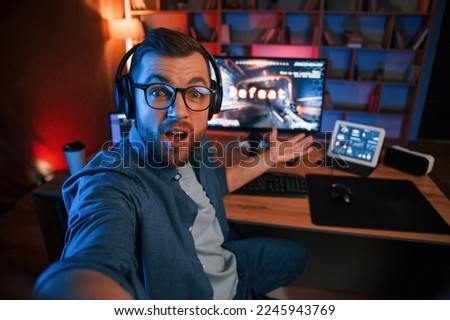 Man is playing the shooter game on his computer. Neon lighting.