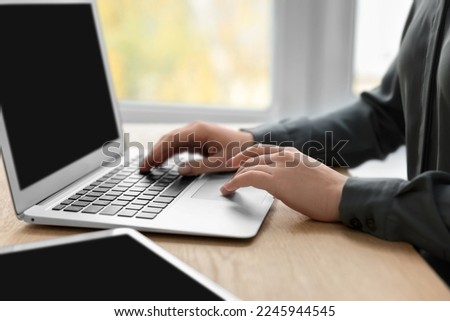 Woman with tablet working on laptop at wooden table, closeup. Electronic document management