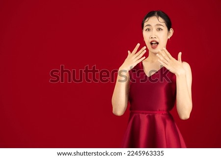 Asian woman wear red elegant dress posing surprised face on red color background.