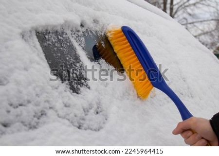 Cleaning the car from snow in winter. A man cleans the windshield of a car from snow.