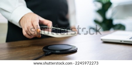 Charging mobile phone battery with wireless charging device in the table. Smartphone charging on a charging pad. Mobile phone near wireless charger Modern lifestyle technology  Royalty-Free Stock Photo #2245972273