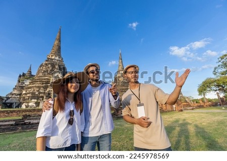 Thai local tour guide is explaining the history of old Siam to the couple of tourist on their backpacker honeymoon travel to ancient temple of Ayutthaya, Thailand Royalty-Free Stock Photo #2245978569