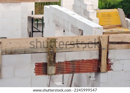 A house under construction, walls made of acc blocks, rough windows and door openings, reinforced brick lintels, a scaffolding, a wooden formwork