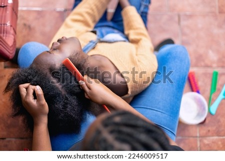Young African girl braiding sister's hair at home while enjoying time together. Black healthy afro hair culture and Style. Royalty-Free Stock Photo #2246009517