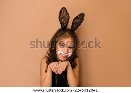 A beautiful funny girl with curly hair and lace ears depicts a rabbit with folded paws .  Animal makeup mask painted with paints on the face . the year 2023 of the hare