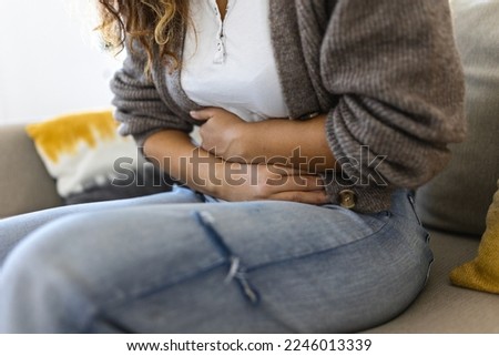 Woman in painful expression holding hands against belly suffering menstrual period pain, lying sad on home bed, having tummy cramp in female health concept Royalty-Free Stock Photo #2246013339