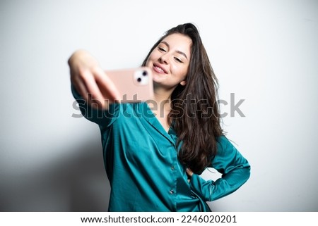 Young brunette attractive girl in casual green silk shirt taking selfie smiling with dimples widely and happily at the camera, blogging