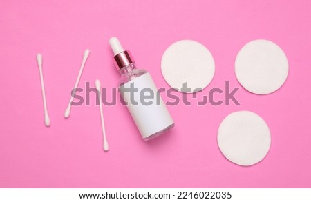 Face serum bottle, cotton pads and sticks on pink background. Facial skin care, hygiene. Flat lay composition