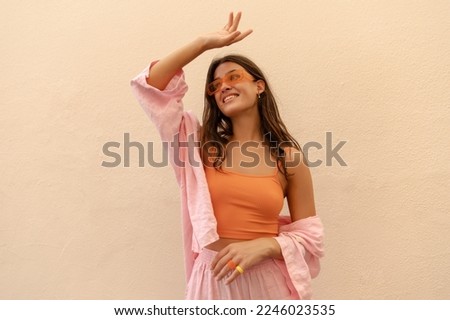 Pretty young caucasian woman looks away laughing streches hand up spends time outside. Brunette wears casual spring clothes. Leisure lifestyle concept.  Royalty-Free Stock Photo #2246023535