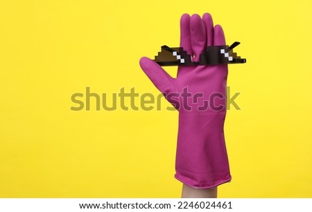 Hand in purple rubber cleaning glove with 8 bit pixel sunglasses on a yellow background. House cleaning and housekeeping concept