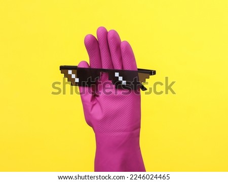 Hand in purple rubber cleaning glove with 8 bit pixel sunglasses on a yellow background. House cleaning and housekeeping concept