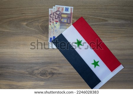 syrian flag on top of coins, placed on wooden background.