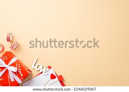 St Valentine's Day concept. Top view photo of red giftbox with ribbon bow envelope with letter hearts decorative tape and inscription love on isolated pastel beige background with copyspace