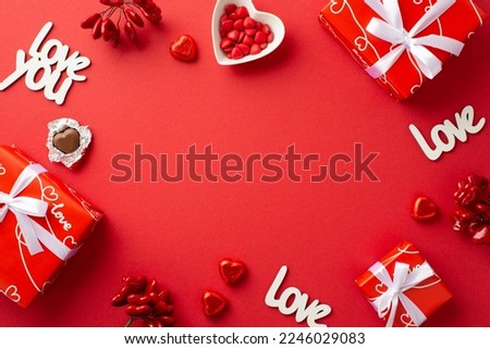 Valentine's Day concept. Top view photo of present boxes with bows heart shaped saucer with sprinkles chocolate candies inscriptions love on isolated red background with blank space in the middle