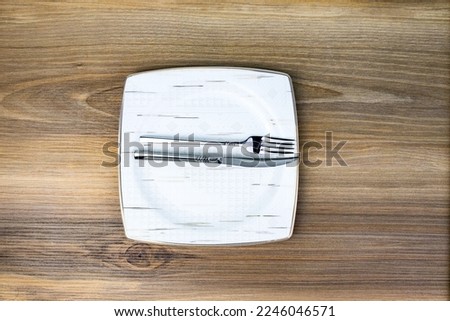 White porcelain plate with fork and knife placed on wooden background meaning I finished my meal and it was amazing.