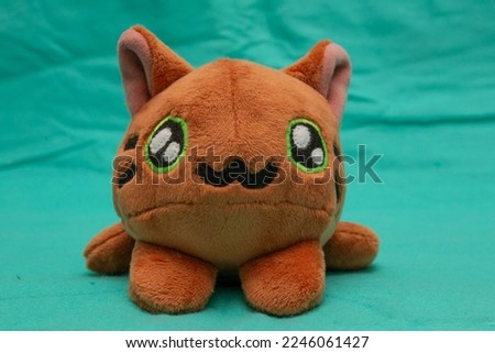 A plush toy cat sewn by hands in golden color lies on a light green background.