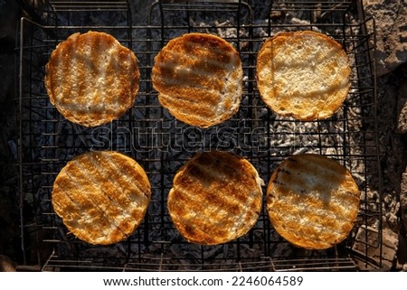 Round buns, lying in rows on the metal grid of the wood-fired grill. The concept of cooking, frying hamburgers. Coal and heat. Top down view.