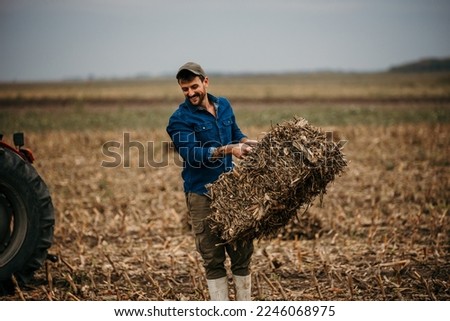 Good looking hard working man wearing boots and a shirt grabs a hay bale stacked in the western barn. Royalty-Free Stock Photo #2246068975
