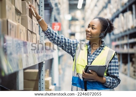 Portrait of young attractive African American woman auditor or trainee staff work looking up stocktaking inventory in warehouse store by computer tablet and headphones near products shelf. Call center Royalty-Free Stock Photo #2246072055