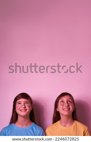 Smiling caucasian teenage girls with colorful sequins on faces look up. Girlfriends of zoomer generation. Modern youngster lifestyle. Friendship. Isolated on pink background. Studio shoot. Copy space