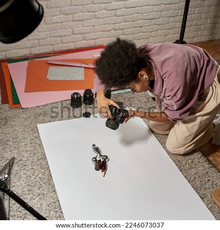Black female photographer taking photo of massager and oil bottles on camera at home studio. Creating beauty and body care content for photostocks, commerce and advertising. Freelance and remote work