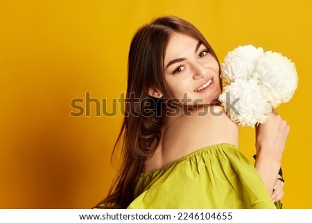 Portrait of young beautiful girl in cute dress posing with flowers over yellow background. Concept of celebration, party, women's day, emotions, holiday, birthday, happiness. Ad