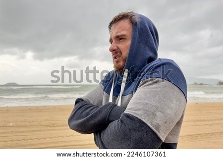 Portrait of unhappy depressed frozen trembling guy, young shivering from cold sad upset man on the sea beach, suffering from bad weather on summer vacation  Royalty-Free Stock Photo #2246107361