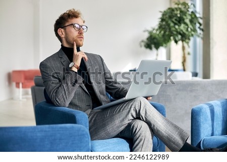 Pensive businessman working using laptop planning startup  sitting in modern office. Portrait of young confident freelancer sitting at workplace