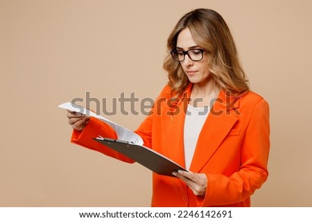 Side view young employee business woman corporate lawyer wears classic formal orange suit glasses work in office hold clipboard with paper account check documents isolated on plain beige background Royalty-Free Stock Photo #2246142691