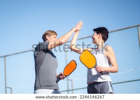 Laughing couple playing pickleball game, hitting pickleball yellow ball with paddle, outdoor sport leisure activity, celebrating victory . Royalty-Free Stock Photo #2246146267