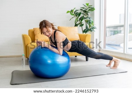 Asian woman, attractive and young, wearing black gym clothes is exercising, toning leg muscles with a blue exercise ball, to health care and exercise in home concept.