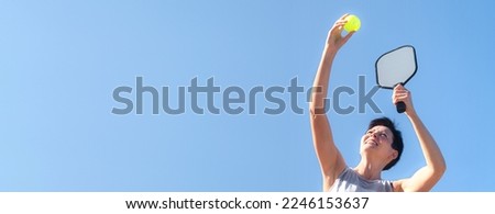 Pickleball banner over blue sky, woman playing pickleball game, hitting pickleball yellow ball with paddle, outdoor sport leisure activity, copyspace for text. Royalty-Free Stock Photo #2246153637