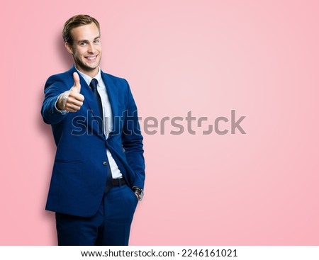 Excited businessman showing thumb up like sign gesture, in blue confident style suit, over rose pink colour background. Handsome happy man. Copy space for slogan or text.