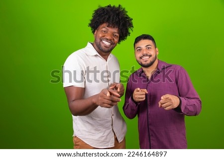 Hey you. Portrait of cheerful male friends pointing two index fingers at camera, isolated over green studio background wall. Young positive friends choosing and indicating