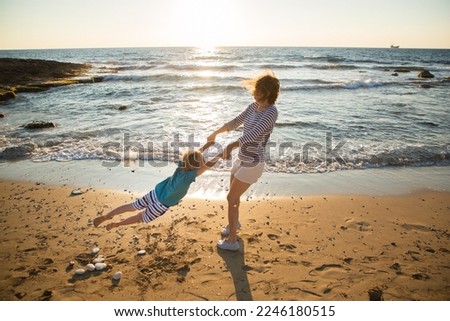 woman is circling the hands of a little boy, mom and son are having fun on the beach at sunset. Joint fun pastime on vacation, the joy of childhood and motherhood. active lifestyle Royalty-Free Stock Photo #2246180515