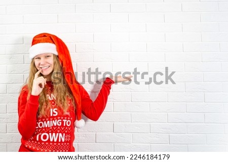 Photo of positive girl wearing santa claus hat hold hand demonstrate christmas new year promotion promo touch teeth fingers wear warm winter clothes. High quality photo