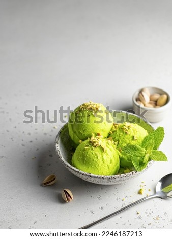 Pistachio ice cream scoop garnished with chopped pistachios and mint with silver spoon on gray textured background, text space. Vertical orientation Royalty-Free Stock Photo #2246187213