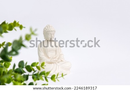 Buddha figurine surrounded by green leaves on a white background. Mental health and meditation concept. Selective soft focus.