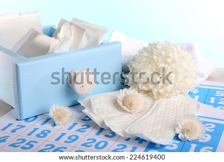 Sanitary pads in box and sanitery pads and white flowers on blue calendar on light blue background