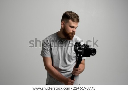 Side view of professional bearded videographer, cinematographer, cameraman using camera on gimbal stabilizer, steadicam on white background. Royalty-Free Stock Photo #2246198775