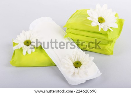 Sanitary pads and white flowers on light background