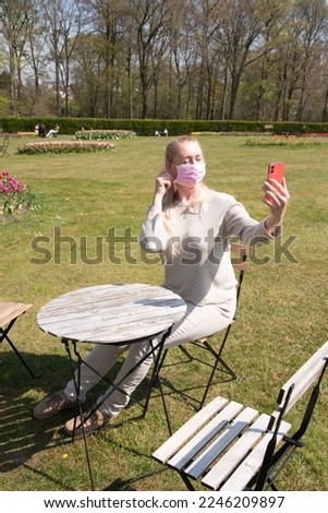 young woman in a protective mask takes a selfie with blooming sprimg tulips
