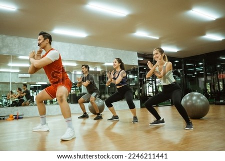 male instructor doing squats together with body combat participants in the fitness center Royalty-Free Stock Photo #2246211441