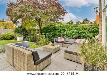 an outdoor living area with wickers and plants on the ground, surrounded by shrubs and trees in springtime