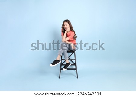 The young adult Asian woman with casual clothes with jeans sitting on the blue background.