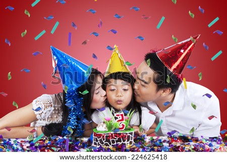 Portrait of little girl blowing candle on birthday cake while kissed by her parents