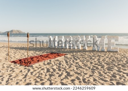 Horizontal photo of "Marry Me" sign at the beach, island on the background. Marriage proposal with red carpet on the sand and torches. Copy space Royalty-Free Stock Photo #2246259609