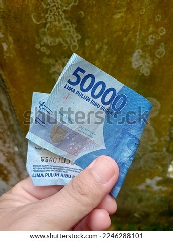 holding fifty thousand rupiah notes. Indonesian currency in 2023